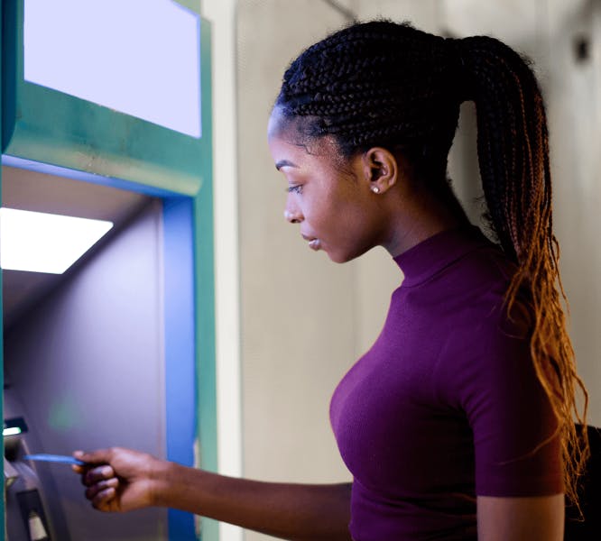 A woman approaching an ATM with her bank card