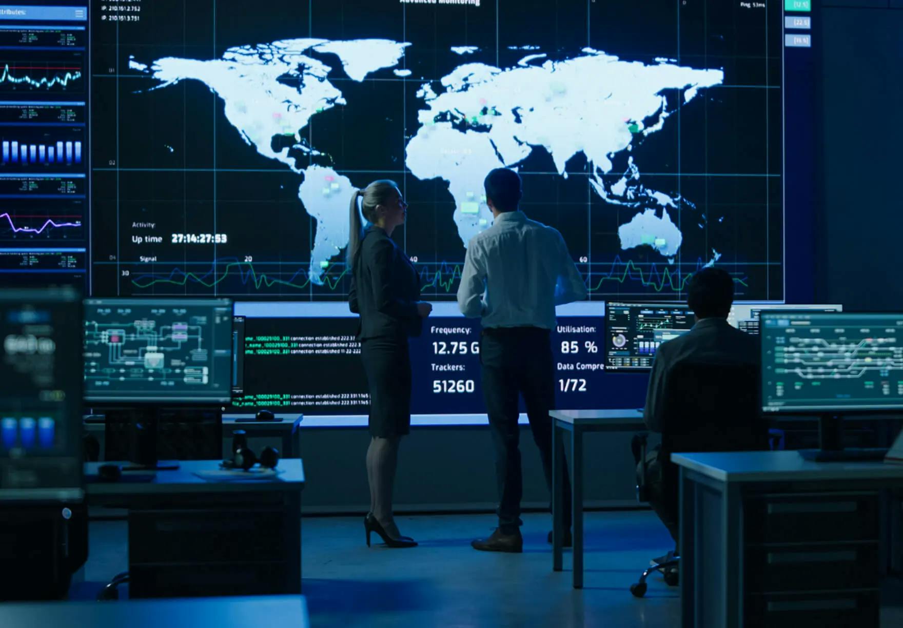 Two workers looking at a large projected computer screen of a world map