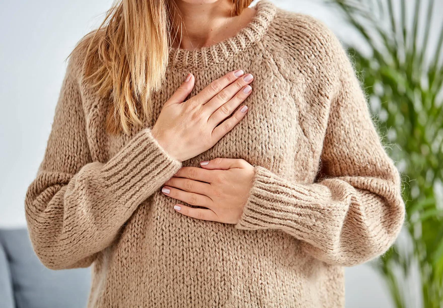 A woman is holding her stomach in a sweater.