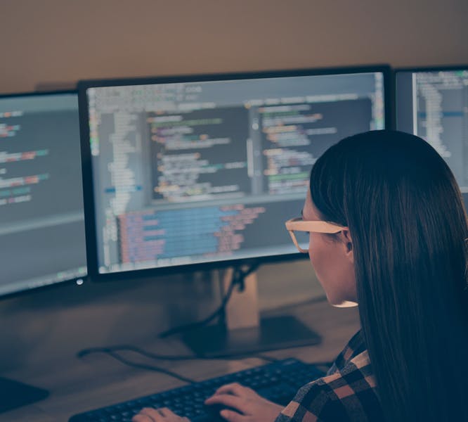 A female remote worker editing form code across multiple desktop monitors