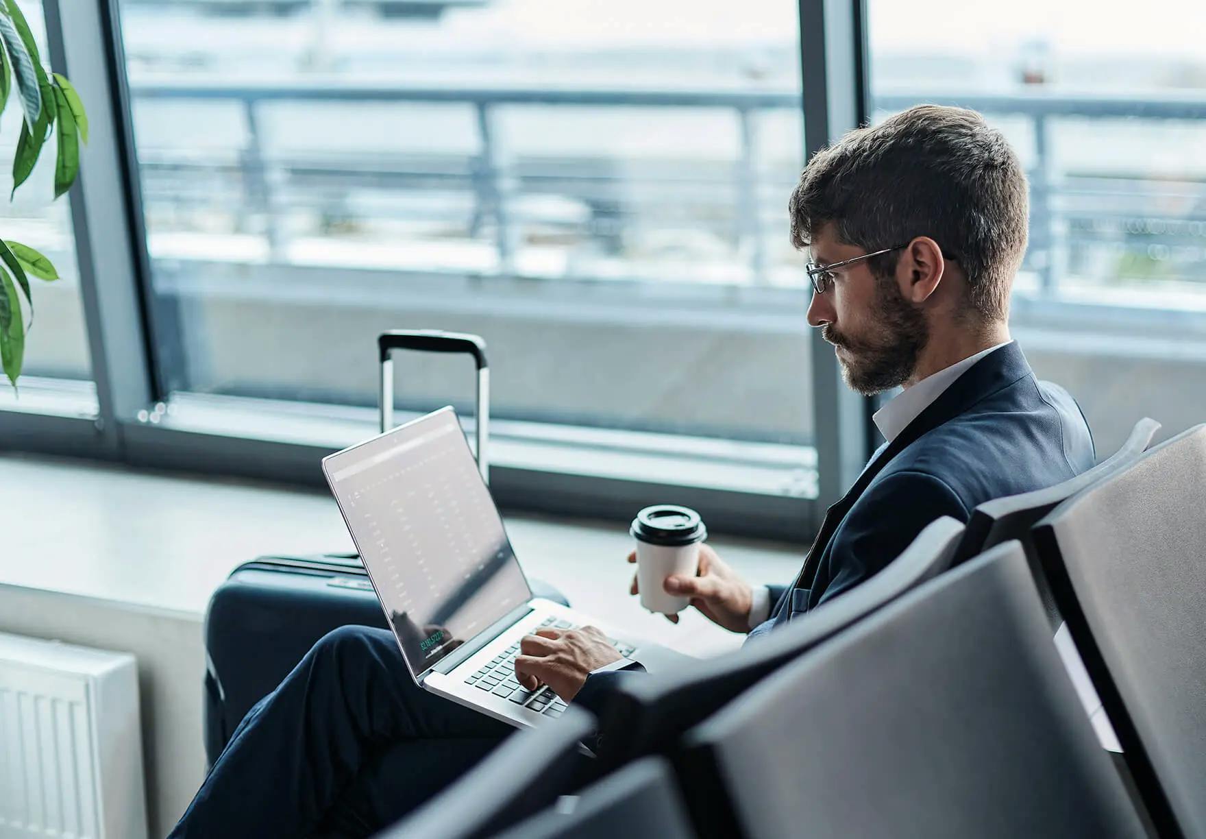 a person working on a laptop and holding coffee at an airport