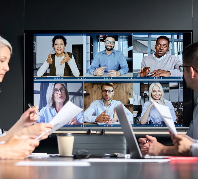 A hybrid HR work team pictured in an office on a video call with a remote team of six employees
